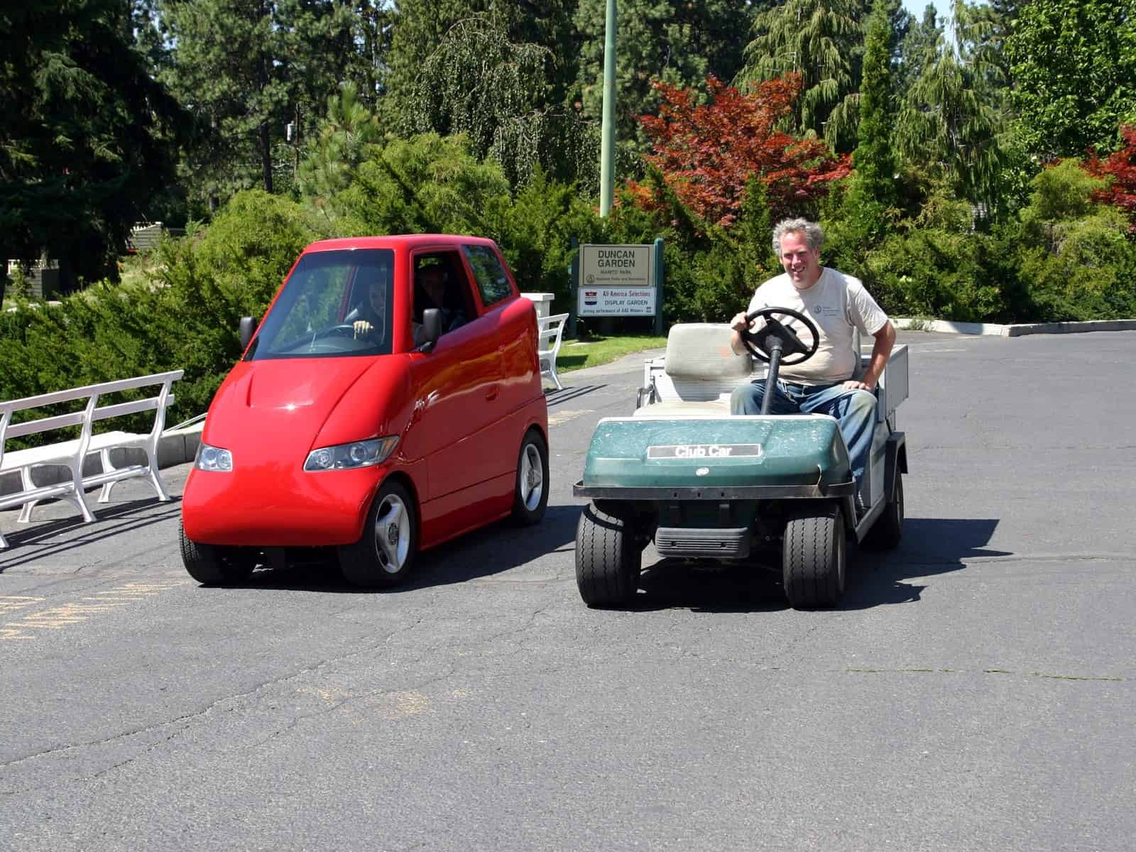 imagem mostra o carro tango, que é fino e vermelho, ao lado de um carrinho de golfe