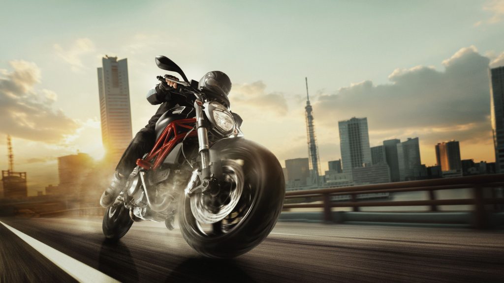 Motociclista acelera pela estrada da cidade ao pôr do sol, inclinando-se na curva com arranha-céus ao fundo