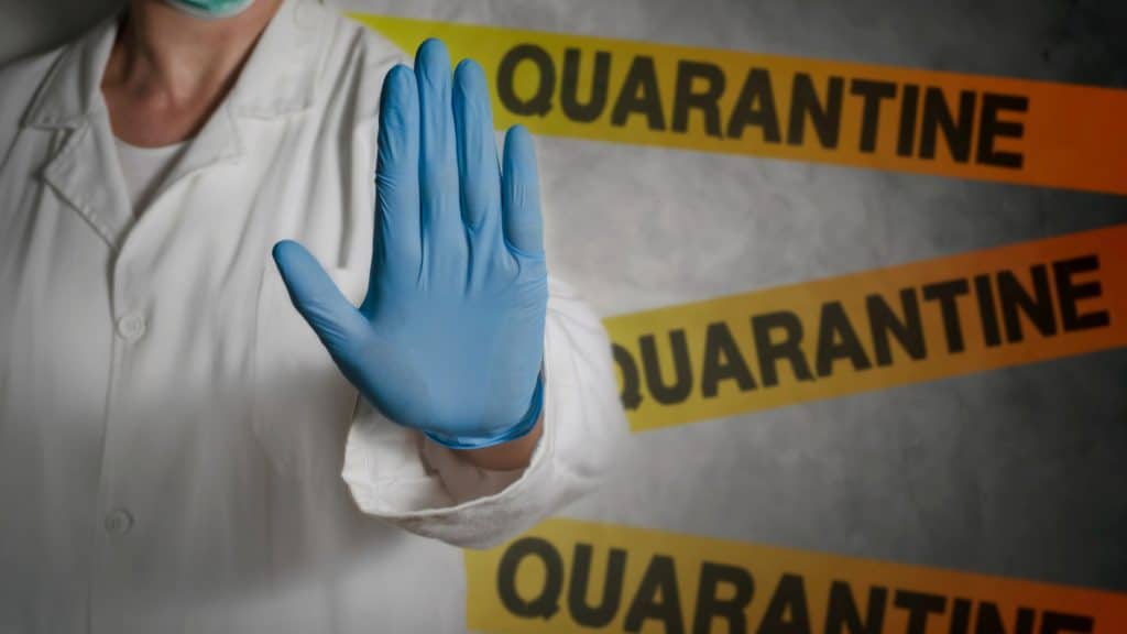 Imagem mostra a mão de um médico impedindo a passagem de uma pessoa, com faixas de passagem proibida atrás dele